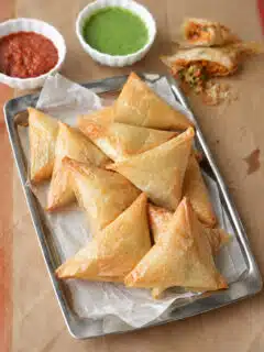 Golden fried Keema Samosa triangles arranged on a plate with tamarind chutney and fresh cilantro.