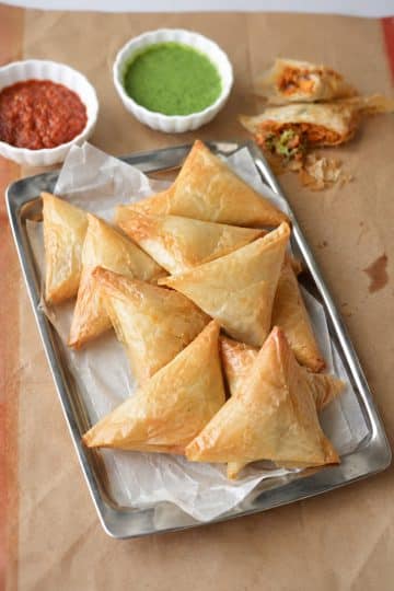 Golden fried Keema Samosa triangles arranged on a plate with tamarind chutney and fresh cilantro.