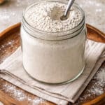 Grainy homemade uttapam mix in a round jar with spoon and flour sprinkled around