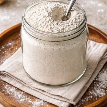 Grainy homemade uttapam mix in a round jar with spoon and flour sprinkled around