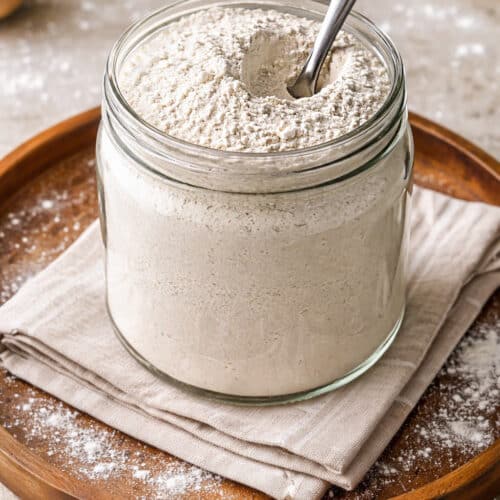 Grainy homemade uttapam mix in a round jar with spoon and flour sprinkled around