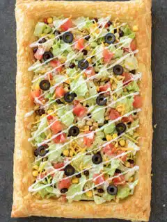 Easy Puff Pastry Taco Pizza topped with lettuce, tomatoes, olives, cheese, and sour cream