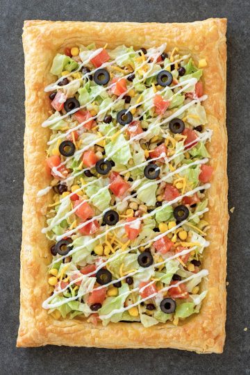 Easy Puff Pastry Taco Pizza topped with lettuce, tomatoes, olives, cheese, and sour cream