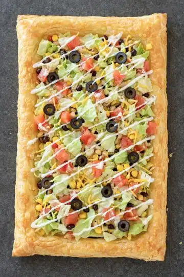 Easy Puff Pastry Taco Pizza topped with lettuce, tomatoes, olives, cheese, and sour cream