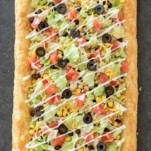 Easy Puff Pastry Taco Pizza topped with lettuce, tomatoes, olives, cheese, and sour cream