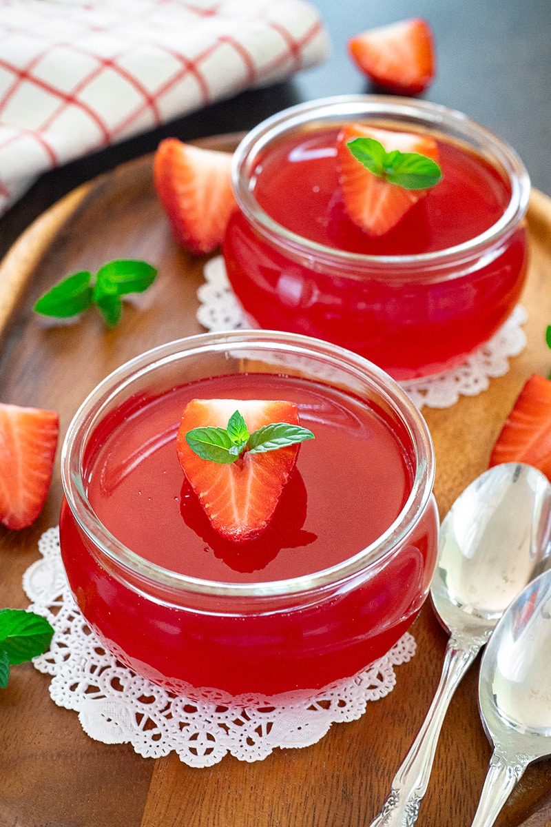  Two bowls of strawberry jello on a wooden tray, garnished with a mint leaf.