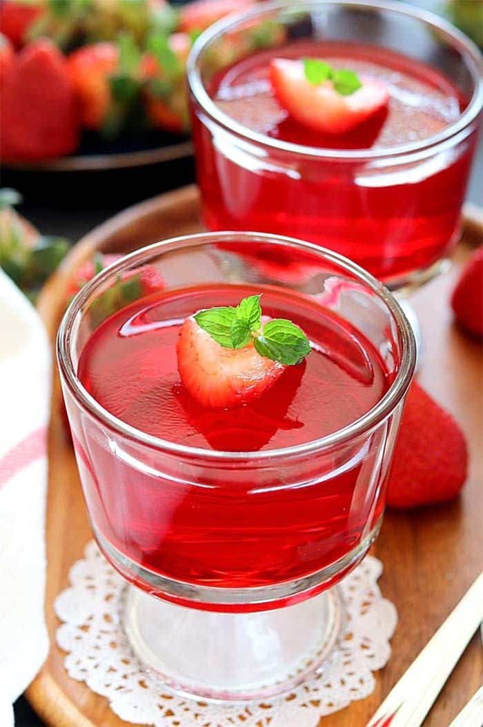 Vegan Strawberry Jelly set in serving cups on a wooden tray, topped with a mint leaf.